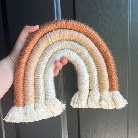Handmade Macrame Apricot Rainbow measuring approximately 10" x 7" and includes a sawtooth hanger on the back to hang on a wall.
